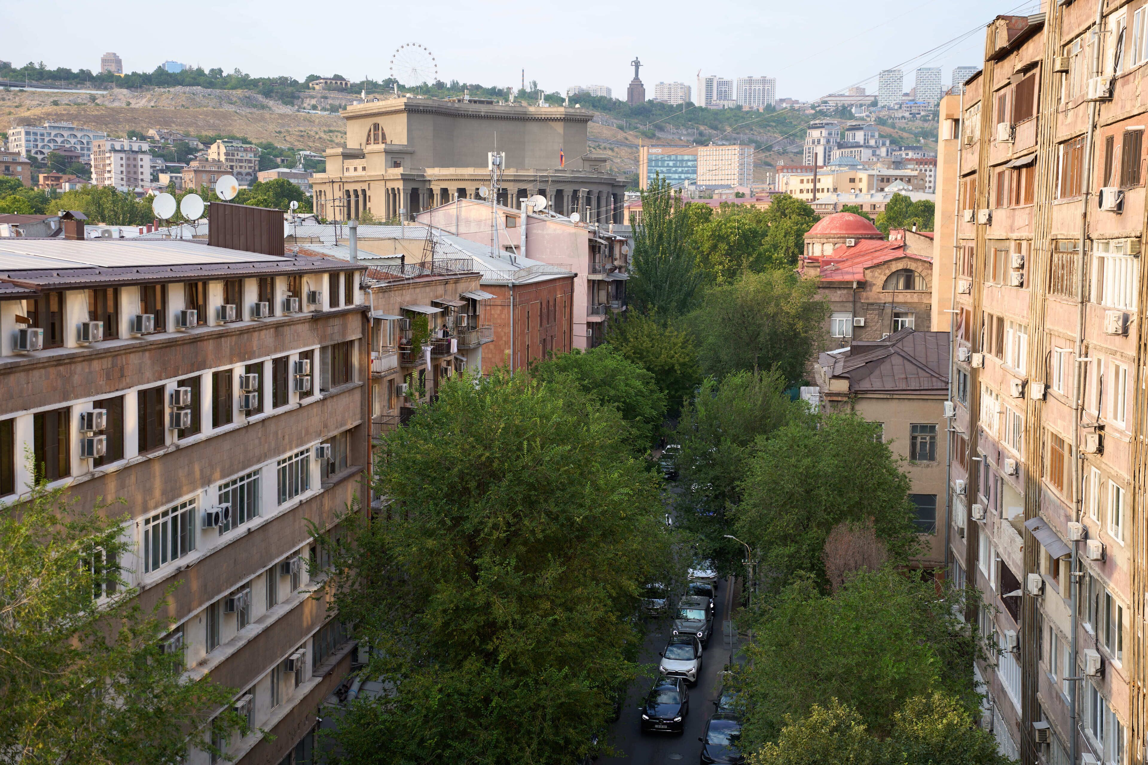 A narrow urban street lined with multi-story buildings, some with visible air conditioning units.