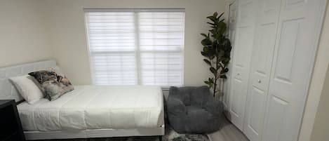 A bedroom with a bed, a nightstand, a plant, and a wardrobe.