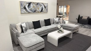 A modern living room with a grey sectional sofa, white ottomans, a white coffee table, and a large abstract painting on the wall.