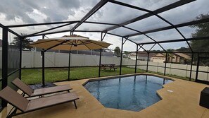 A backyard swimming pool with a covered patio area, including a table and chairs.