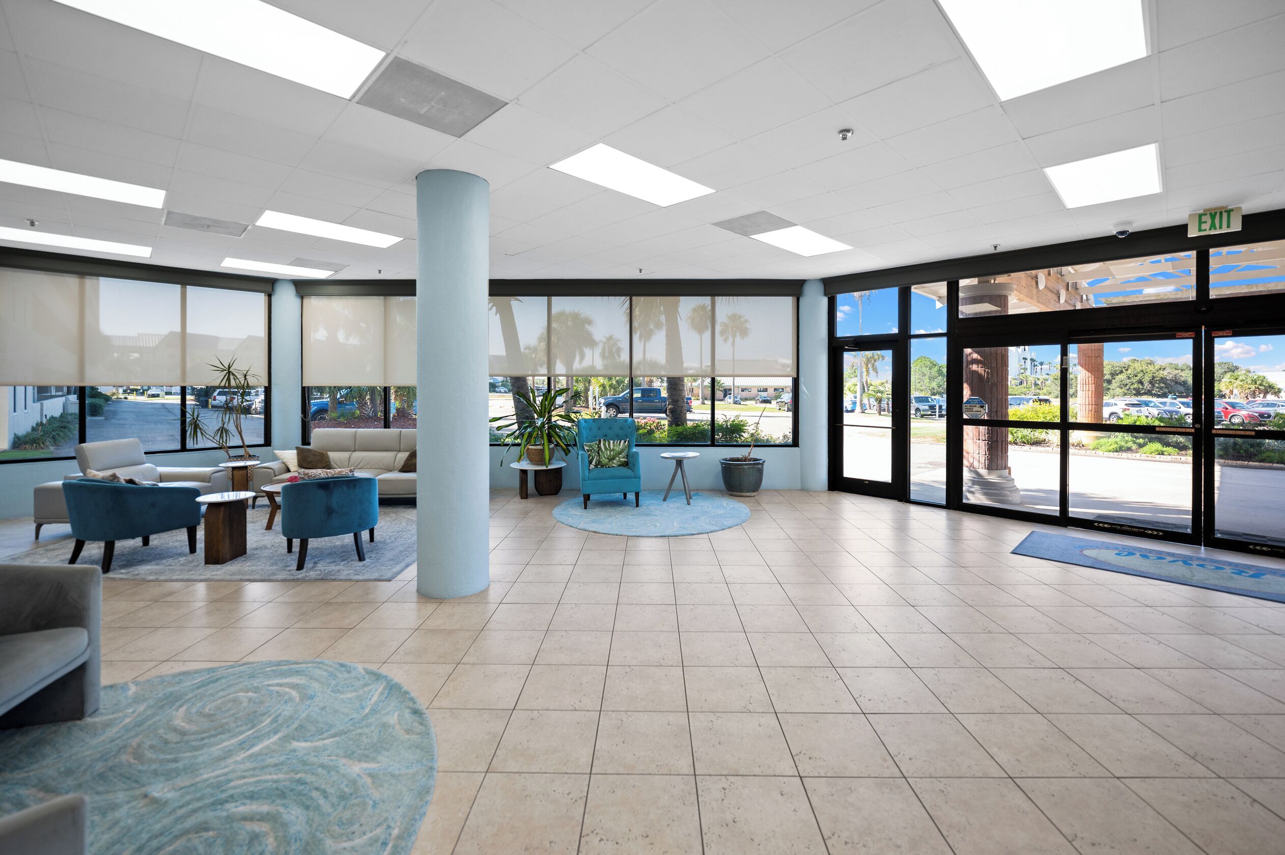 A spacious lobby with a large column, seating area, and large windows offering a view of the parking lot.