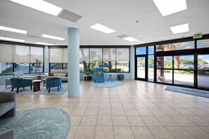 A spacious lobby with a large column, seating area, and large windows offering a view of the parking lot. - Remodeled 2BR Condo | Beach Access & Pools | Penthouse Gulf Views (Gulf Shores)