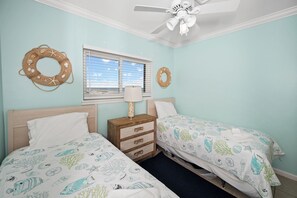 Ein Schlafzimmer mit zwei Betten, einem Deckenventilator, einem Fenster mit Jalousien und dekorativen Wandgestaltungen.