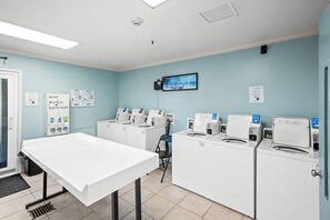 A laundry facility with multiple washing machines, a table, and a chair.