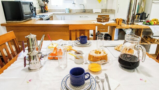 A breakfast setting with a table set for two, including a coffee pot, cups, a plate with orange slices, a cake, and a jug of juice.