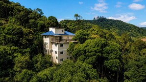 A multi-story building surrounded by dense forest, with a clear sky above.