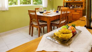 A dining area with a table set for two, a fruit tray with bananas and apples, and a wooden cabinet in the background.