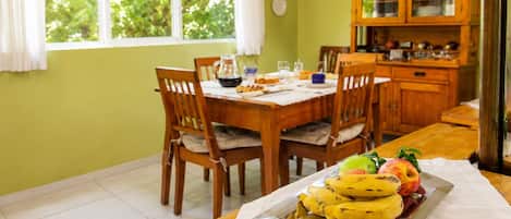 A dining area with a table set for two, a fruit tray with bananas and apples, and a wooden cabinet in the background.