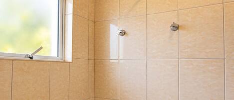 A bathroom with beige tiles, a showerhead, and a window.