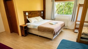 A bedroom with a bed, a bedside table, a window with curtains, and a radiator.