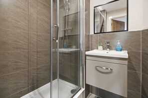 A modern bathroom with a glass shower enclosure, a white sink, and a mirror above the sink. - Modern 2 Bedroom Flat l Manchester city l Sleeps 5 ! (Manchester)