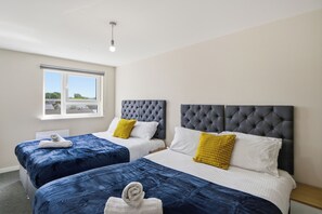 Ein Hotelzimmer mit zwei Betten, jeweils mit einem gesteppten Kopfteil, weißer Bettwäsche und einem gelben Kissen. Ein Fenster bietet Blick ins Freie.