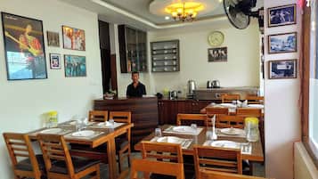 A restaurant with wooden furniture, a receptionist, and wall decorations including framed pictures and a clock.