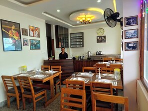 Restaurante com mobiliário de madeira, uma recepcionista e decorações nas paredes, incluindo quadros e um relógio.