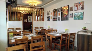 A restaurant interior with wooden tables and chairs, a fan, and wall art.