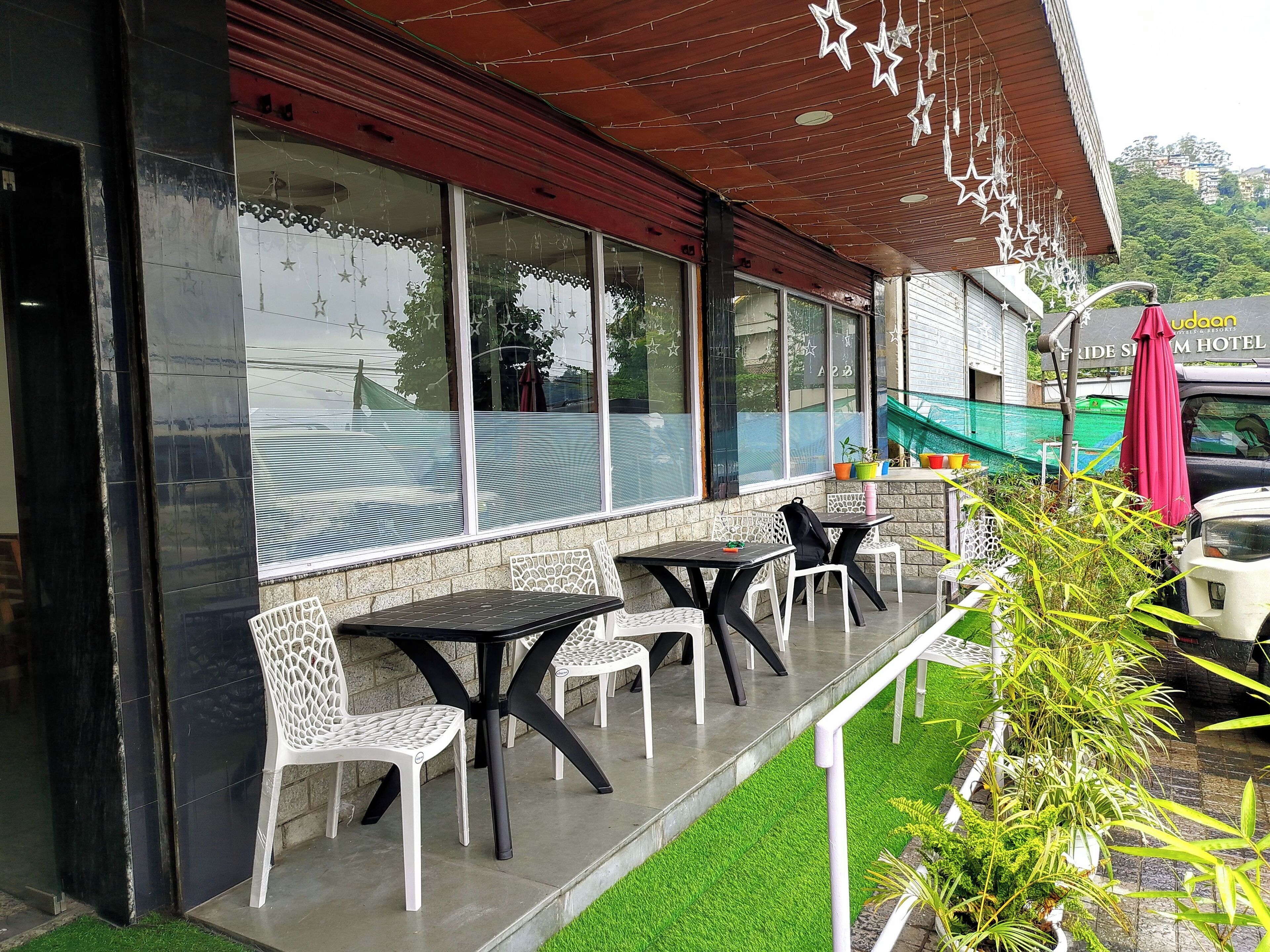 A hotel exterior with outdoor seating, a red awning, and a view of a hill.