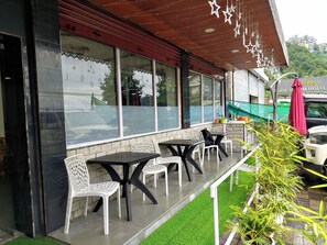 A hotel exterior with outdoor seating, a red awning, and a view of a hill. - Hotel New Empire (Gangtok)