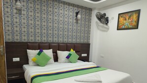 A hotel room with a bed, a headboard, a wall with a geometric pattern, a painting, and a fan. - Hotel New Empire (Gangtok)