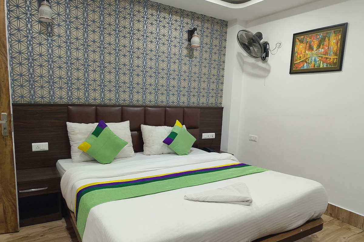 A hotel room with a bed, a headboard, a wall with a geometric pattern, a painting, and a fan.