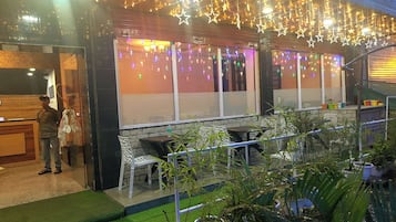 An outdoor seating area with tables and chairs, surrounded by potted plants.