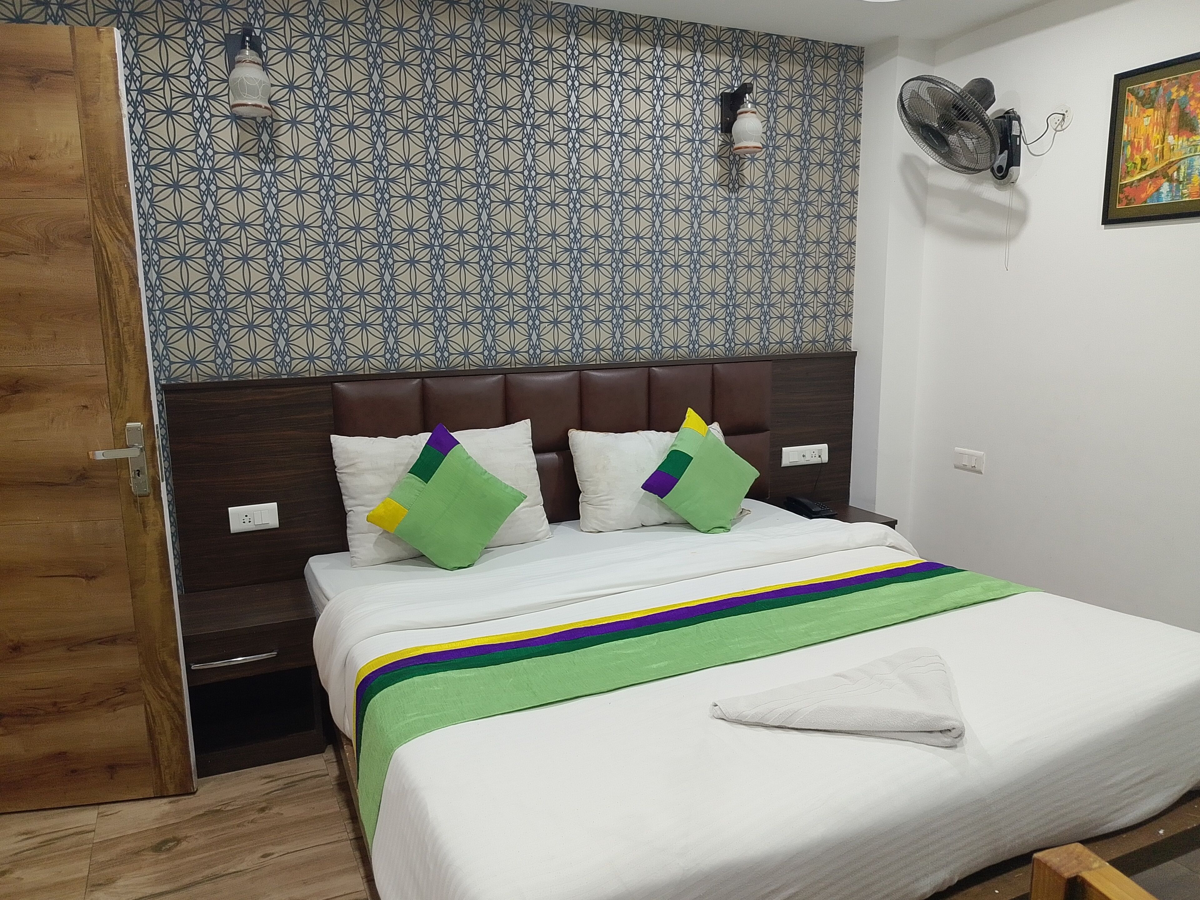 A hotel room with a patterned wall, a bed with a striped bedspread, and a wooden door.