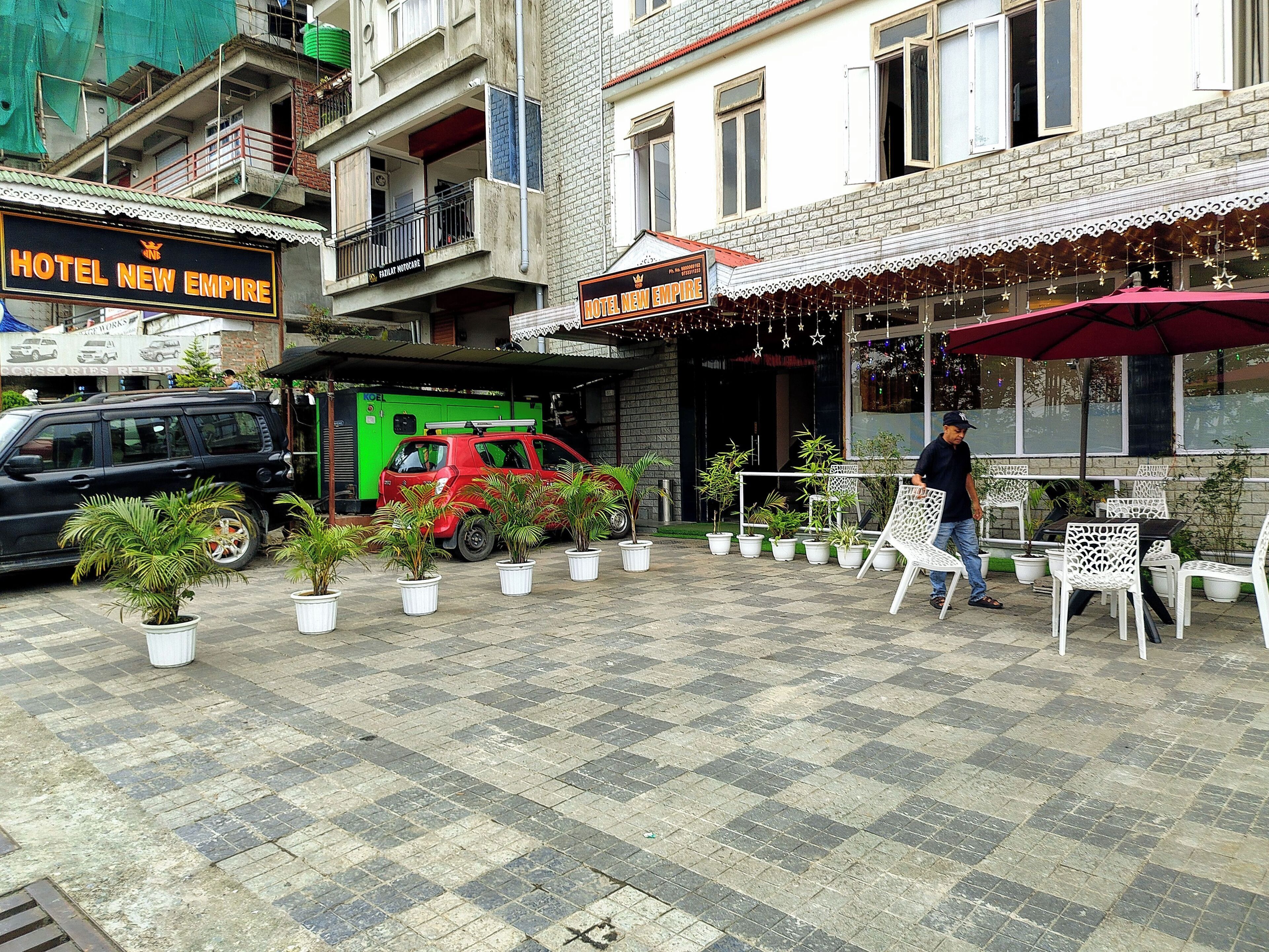 A hotel named 'Hotel New Empire' with a paved outdoor area, potted plants, and outdoor seating.