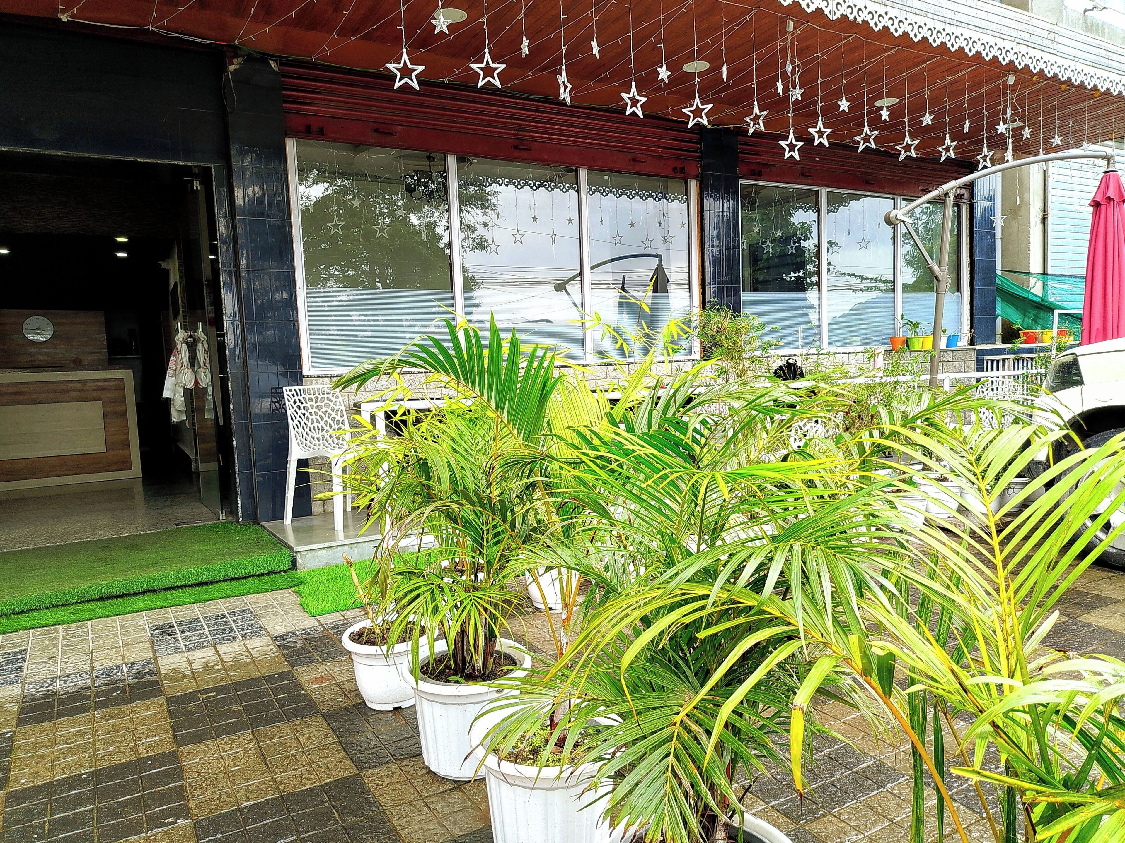 A hotel entrance with a tiled porch, potted plants, and a red awning.