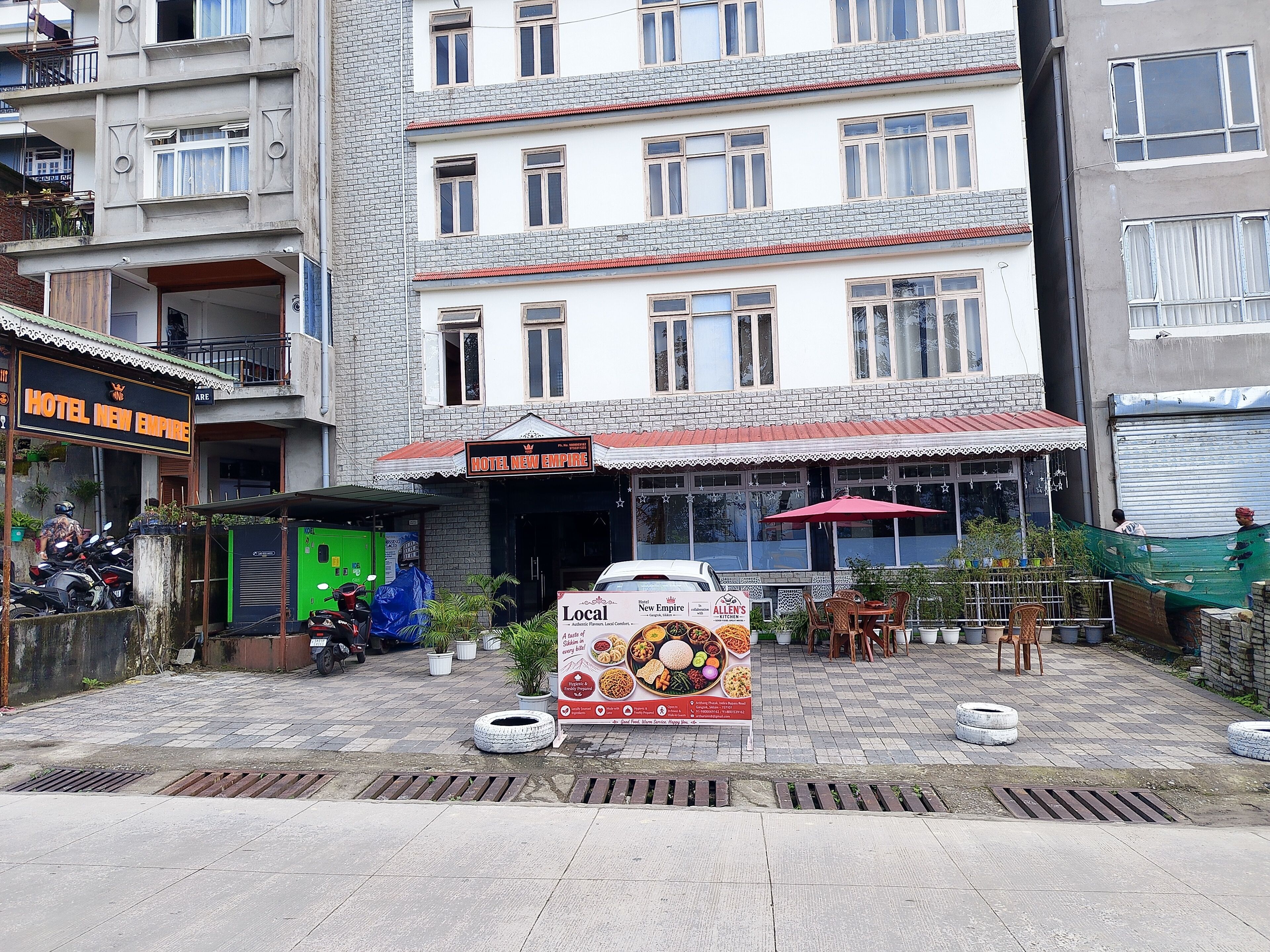 A hotel named 'Hotel New Empire' with a signboard, outdoor seating area, and a parked car.