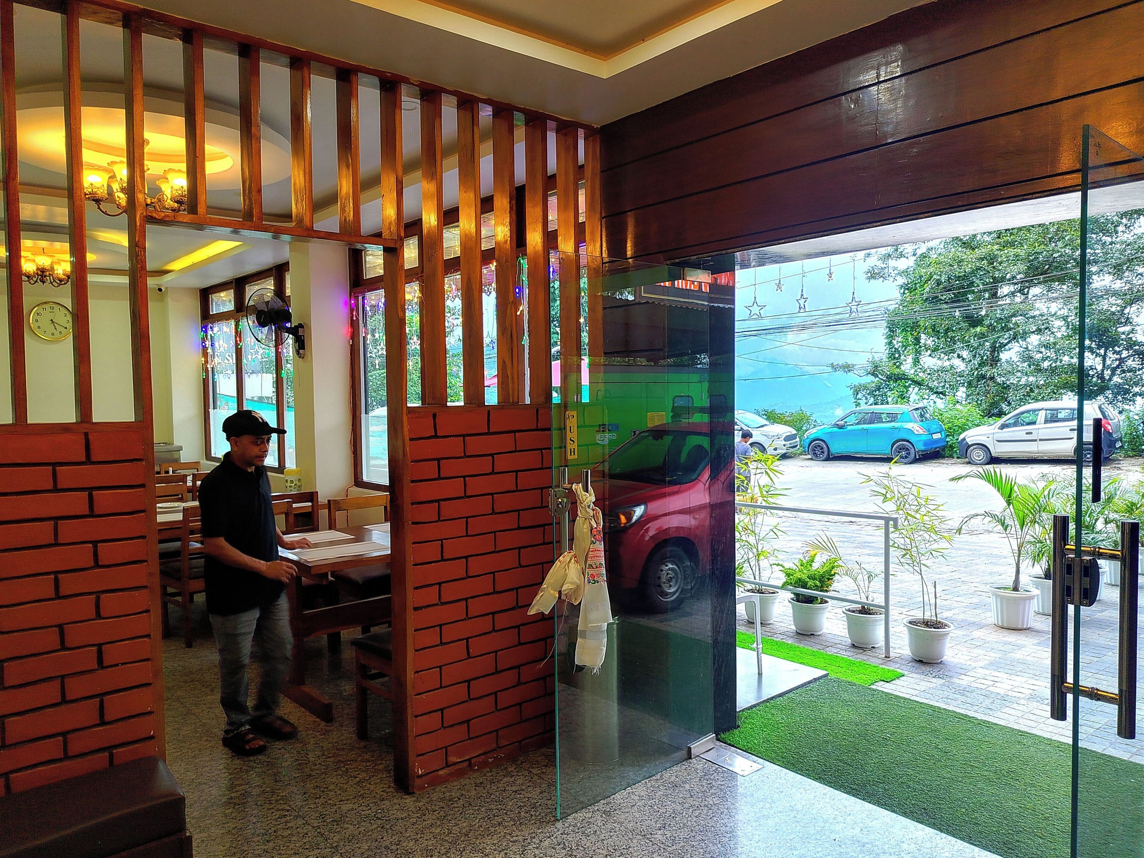 A restaurant with a brick partition, a man standing by the counter, and a view of parked cars outside.