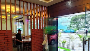 A restaurant with a brick partition, a man standing by the counter, and a view of parked cars outside. - Hotel New Empire (Gangtok)