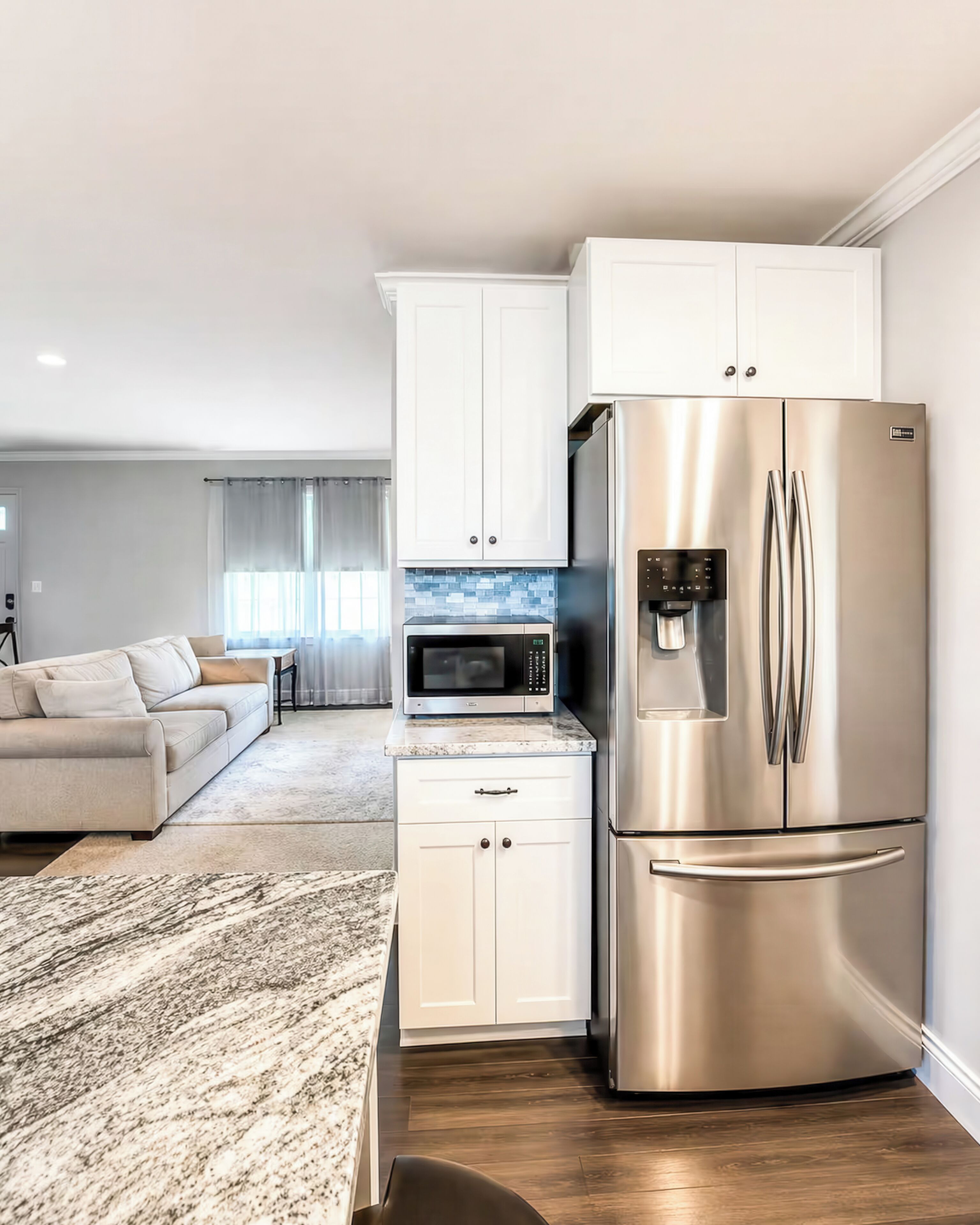 A modern kitchen with white cabinets, a stainless steel refrigerator, a microwave, and a water dispenser.