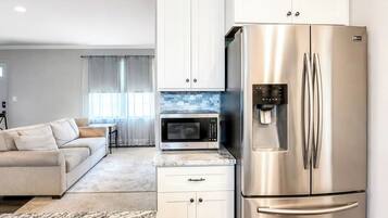 A modern kitchen with white cabinets, a stainless steel refrigerator, a microwave, and a water dispenser.