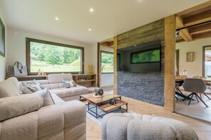 Ein modernes Wohnzimmer mit Kamin aus Stein, großen Fenstern und einer gemütlichen Sitzecke.