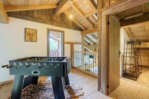 Ein Zimmer mit Tischfußball, Holzbalken, einem großen Fenster und einer Leiter.