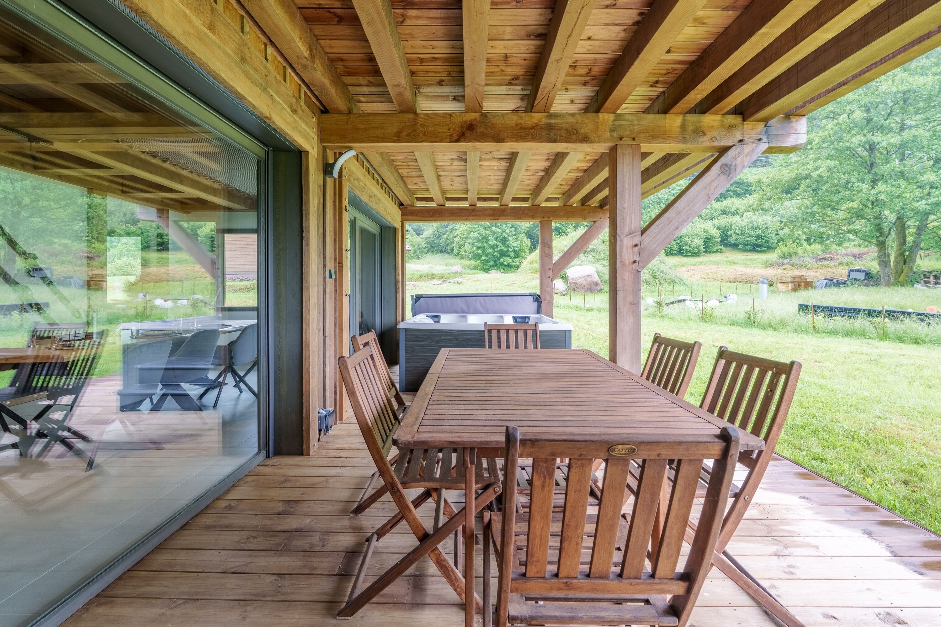 Een terras van hout buiten, met een tafel, stoelen, een barbecue en een glazen deur naar een patio.