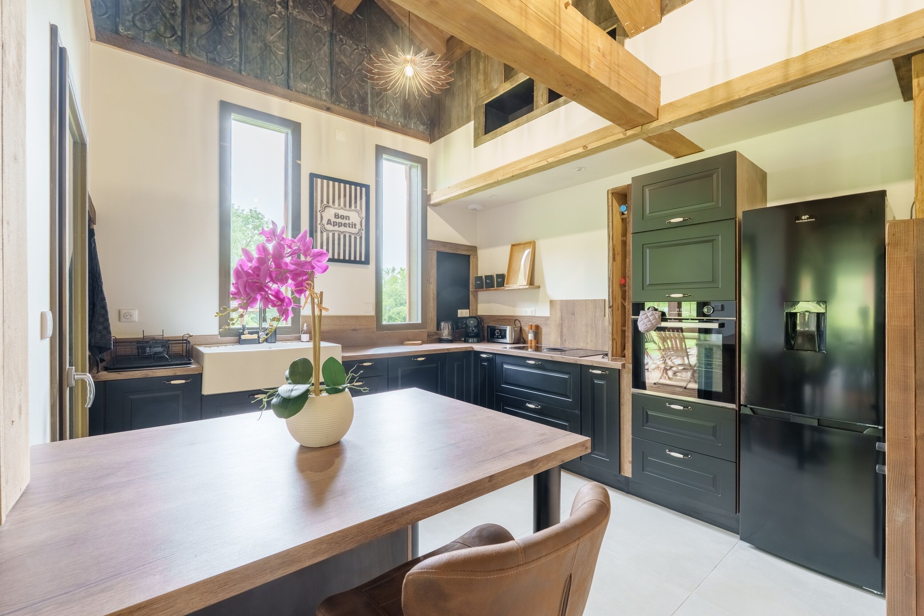 Une cuisine moderne avec des meubles de rangement sombres, une table à manger en bois et un réfrigérateur noir.