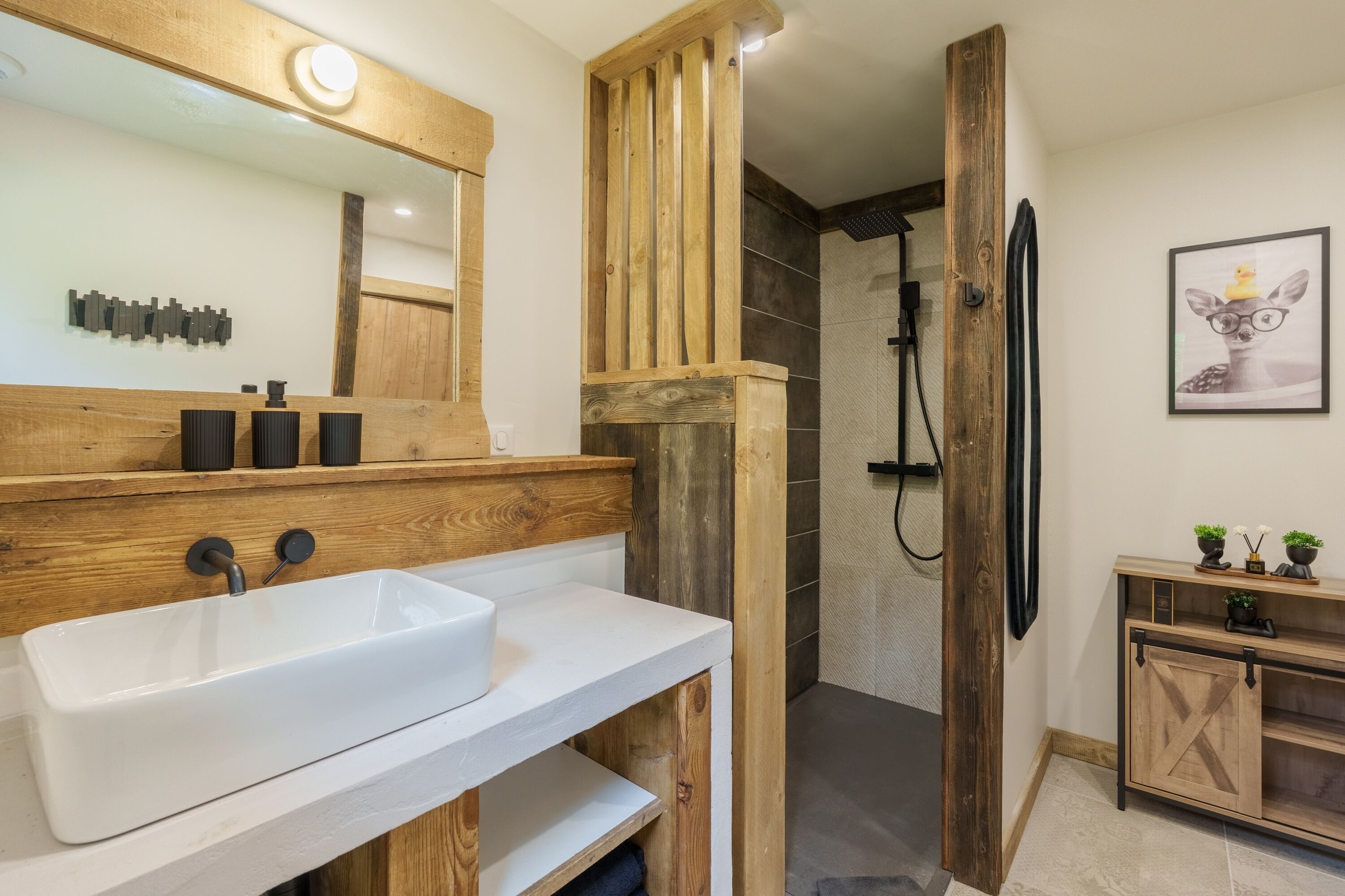 A bathroom with a wooden vanity, a large mirror, a white sink, and a shower area.