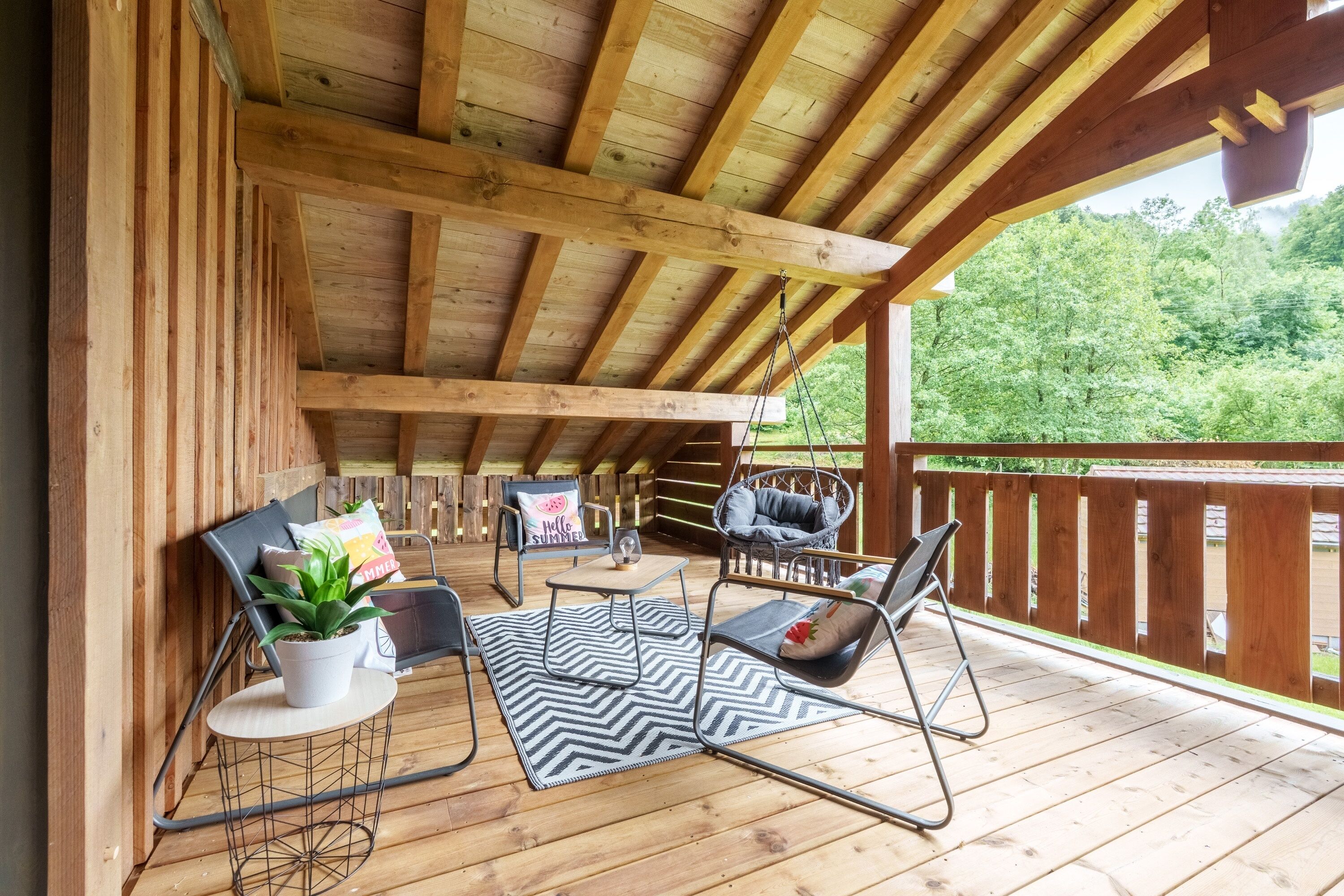 A wooden deck with outdoor furniture, including chairs and a table, under a wooden roof structure.