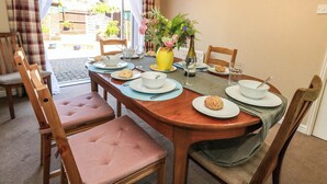Mesa de jantar posta para quatro, com cadeiras, um vaso de flores e uma garrafa de água.