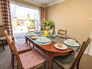 A dining table set for four with chairs, a vase with flowers, and a bottle of water. - Cove Cottage (Weymouth)