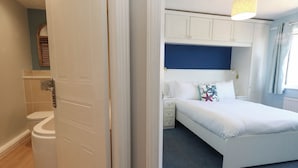 Quarto com cama, mesa de cabeceira, luminária e janela com cortinas.