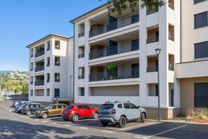 A multi-story residential building with balconies, a parking lot with several cars, and a clear sky. - Le Cocon d'Orezza - Appart Climatisé avec Balcon (Penta-di-Casinca)