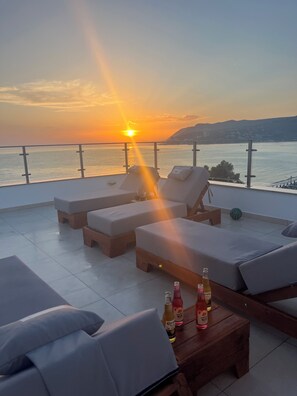 A terrace with lounge chairs and a table with bottles, overlooking a body of water and a distant landscape. -     Beautiful Apartment Near the Beach with Spectacular Sunset ViewsShëngjin (Shëngjin)