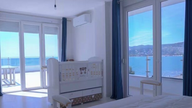 Quarto com cama, penteadeira, cadeira e vista para o mar.