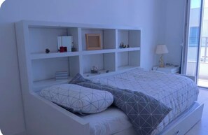Une chambre moderne avec un lit intégré, une table de chevet avec une lampe et une grande fenêtre.