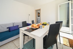 Ein Essbereich mit einem weißen Tisch, schwarzen Stühlen, einem blauen Sofa und einer Tür, die auf einen Balkon führt.