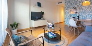 A modern living room with a flat-screen TV, a dining table with chairs, a coffee table with a bottle and glasses, and a potted plant. - Apartment 'La Rosaleda' with Balcony, Wi-Fi and Air Conditioning (Málaga)