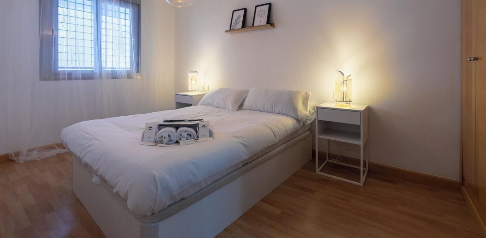 Ein Schlafzimmer mit einem Bett, Nachttischen, einem Fenster mit Vorhängen und einem Regal mit einer Lampe.