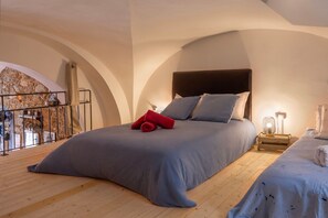 A bedroom with a large bed, a nightstand with a lamp, a balcony with a railing, and a stone wall. - Le Loft de L'Île - A 250m de la Plage (L'Île-Rousse)