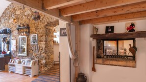 Ein rustikales Interieur mit einer Steinwand, Holzbalken, einem Kamin und einer Sammlung von Büchern und Keramik.